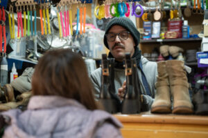 a man in a beanie and glasses looking at a woman in a store